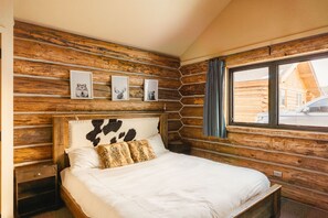 A wooden log cabin room with a bed, framed pictures on the wall, and a window with curtains. - Ski-In/Out Mountain Cabin Home! Private Hot Tub, Stunning Views, 7min Drive to R (Big Sky)