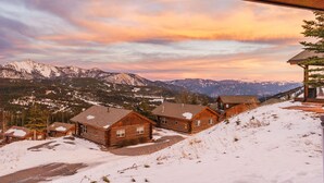 Una hilera de cabañas de madera con vistas a montañas nevadas y un cielo al atardecer.