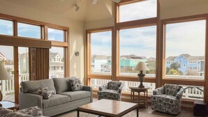 A spacious living room with large windows, a gray sofa, patterned armchairs, and a coffee table. - 1600 - Bases Loaded - Spacious Buck Island Retreat in Corolla (Corolla)