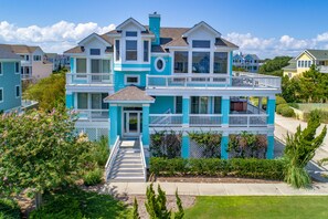 A two-story house with a balcony on the second floor, surrounded by greenery. - 1600 - Bases Loaded - Spacious Buck Island Retreat in Corolla (Corolla)