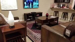 A living room with a sofa, a coffee table, a TV, and a kitchen area with a microwave. - Lackland AFB/Seaworld (1) (San Antonio)