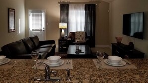 A living room with a sofa, coffee table, TV, and dining area with a granite countertop and chairs. - Lackland AFB/Seaworld (1) (San Antonio)