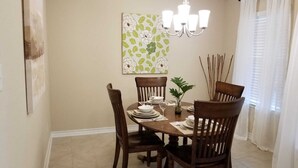 A dining room with a round table, six wooden chairs, a chandelier, and a floral wall hanging. - Lackland AFB/Seaworld (1) (San Antonio)