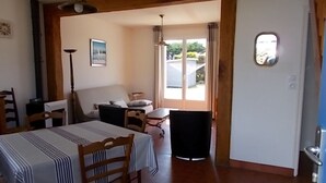 Een eetgedeelte met een tafel voor twee, een stoel, een bijzettafeltje en uitzicht op de omgeving door een glazen deur.