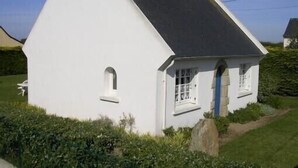 Een wit huis met een steil dak, een klein portaaltje en een raam met een blauwe deur.