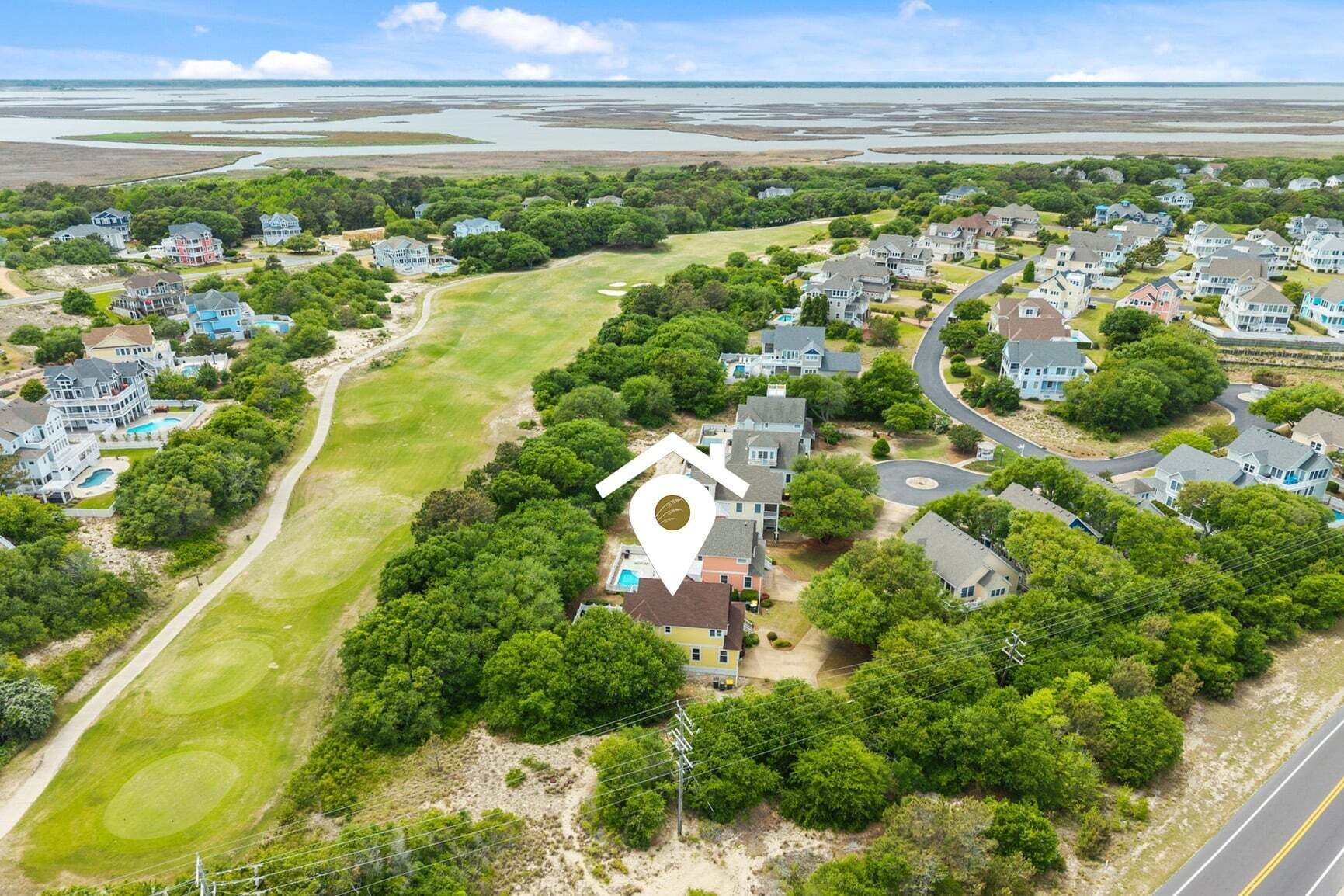 An aerial view of a residential area with houses, a golf course, and a large body of water in the background.