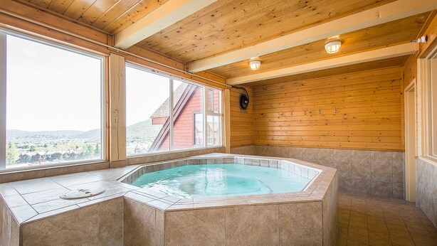 Un bain à remous dans une pièce aux murs en bois et aux grandes fenêtres.