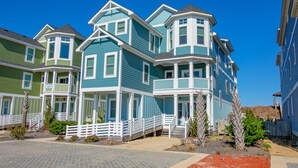A row of blue and green houses with white trim, a paved walkway, and small plants. - 5464- EY BELIEVE - Oceanfront Nags Head | 8BR Luxury Retreat (Nags Head)