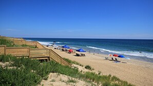 A beach with wooden walkways, blue umbrellas, and people enjoying the shore. - 5464- EY BELIEVE - Oceanfront Nags Head | 8BR Luxury Retreat (Nags Head)