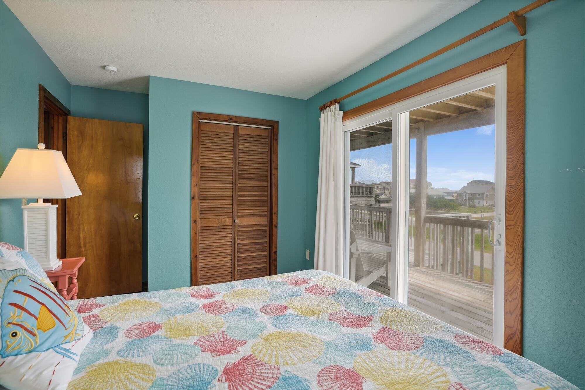 Una camera da letto con un letto, una porta in legno, una finestra con tende e vista su un balcone.