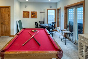 A pool table with pool cues and balls, a dining table with chairs, and a window with a view. - 5405- Adagio - Oceanfront Nags Head | Pool, Hot Tub & Elevator (Nags Head)