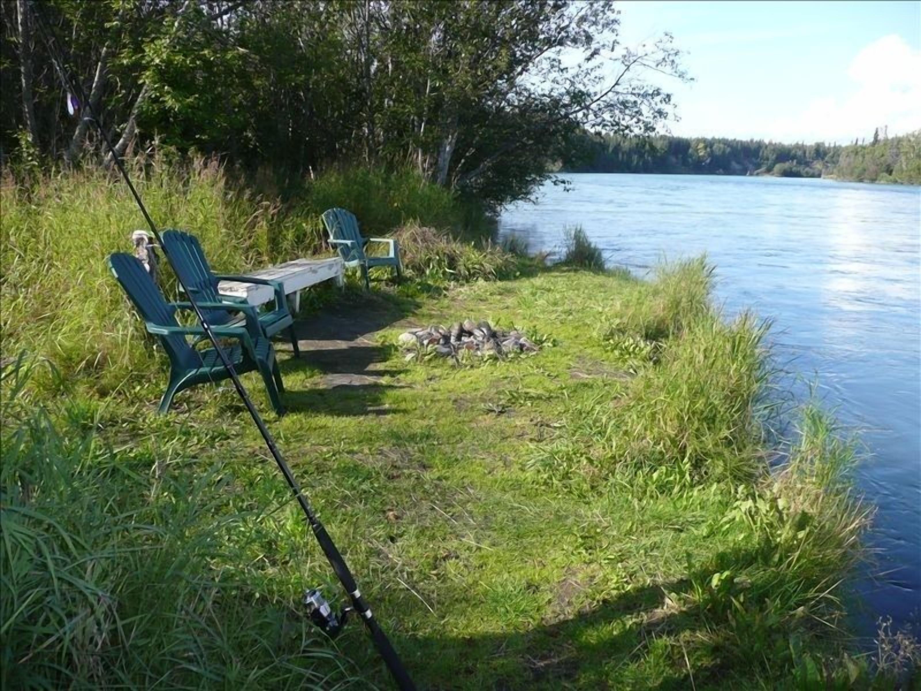 A riverside camping area with chairs and a fishing rod.
