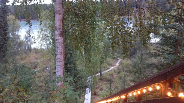A wooden bridge with lights, surrounded by trees and a path leading to a building.