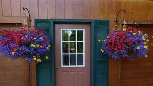 A wooden house with a brown door, green shutters, and hanging flower baskets.
