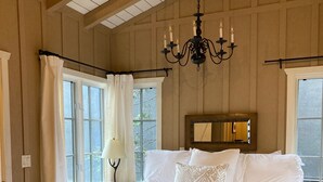 A large bed with white linens, a chandelier, and a window with curtains.