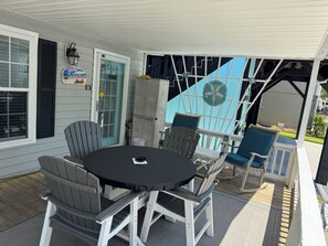 Une terrasse couverte avec une table ronde et quatre chaises, une porte avec une pancarte et une chaise bleue avec un coussin.