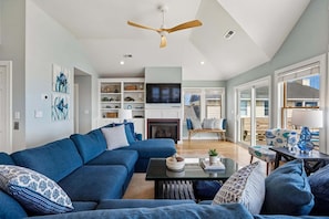 A modern living room with a sectional sofa, a fireplace, a television, and a dining area with a table and chairs.
