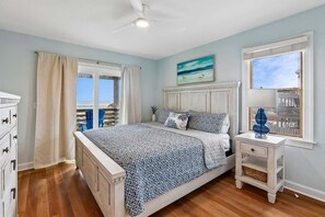 A bedroom with a bed, a nightstand, a dresser, a window with a view, and a ceiling fan. - 5514- Sisterly Love - Luxury Oceanfront | Pool, Hot Tub & Views (Nags Head)