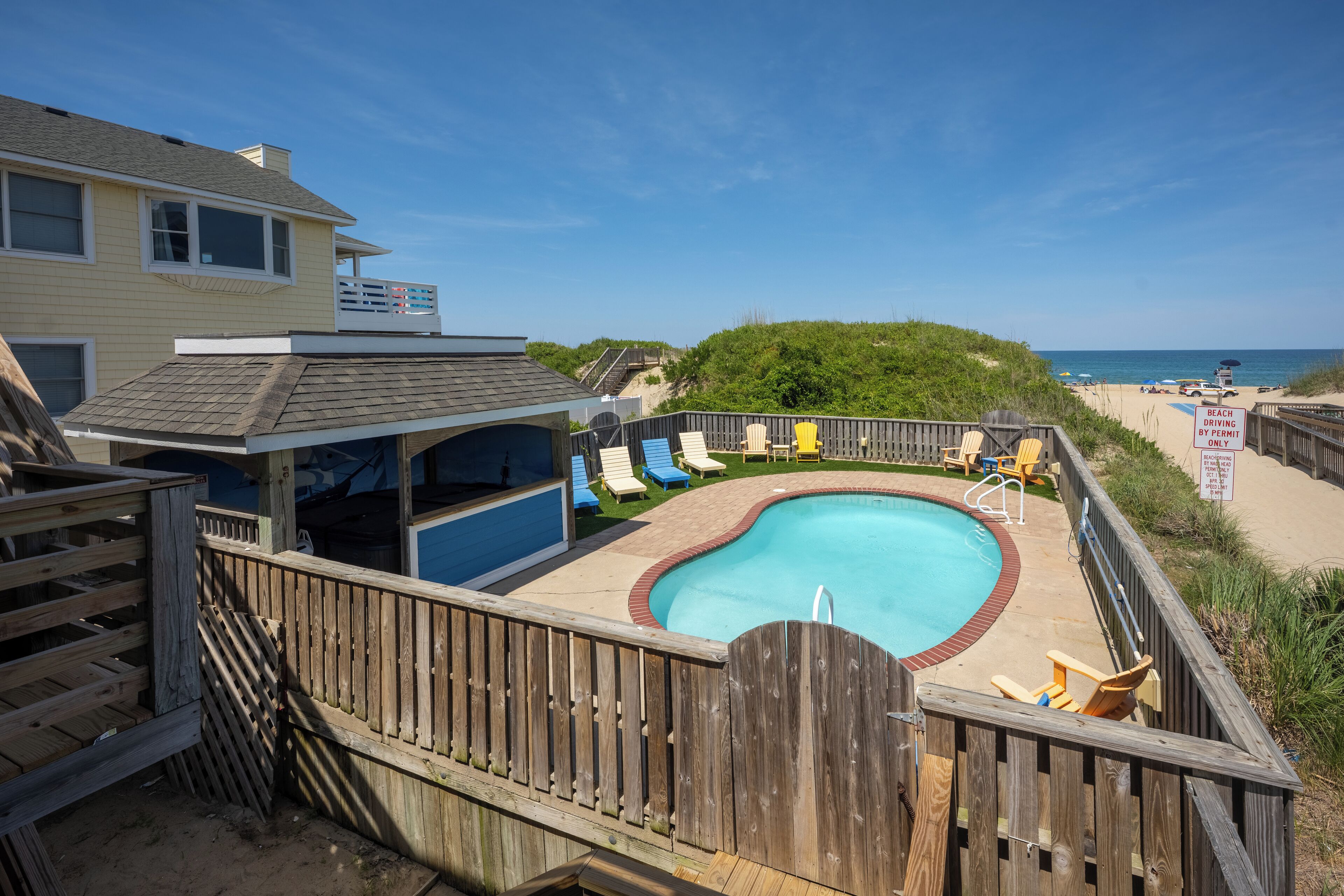 Un patio in legno con piscina, sedie da spiaggia e vista sull'oceano.
