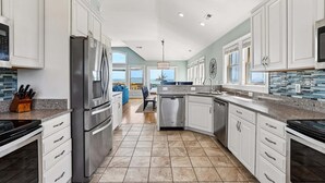 A modern kitchen with white cabinets, stainless steel appliances, and a view to the outside. - 5514- Sisterly Love - Luxury Oceanfront | Pool, Hot Tub & Views (Nags Head)