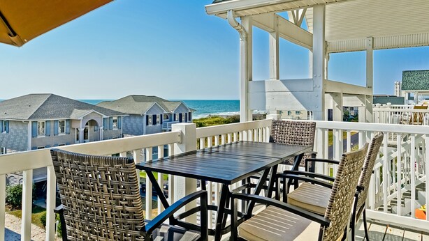 A balcony with a table and chairs, overlooking a beach and houses. - Gorgeous 4 BR/4 BA Top Floor Front Row Islander Villa (Ocean Isle Beach)