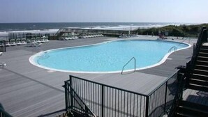 A pool with a view of the ocean, surrounded by lounge chairs and a wooden deck. - Gorgeous 4 BR/4 BA Top Floor Front Row Islander Villa (Ocean Isle Beach)