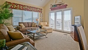 A spacious living room with a large window, a ceiling fan, and a view of the city. - Gorgeous 4 BR/4 BA Top Floor Front Row Islander Villa (Ocean Isle Beach)