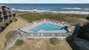 A pool area with a view of the ocean, surrounded by a wooden deck and a building with multiple balconies. - 3196 - Sea Sights - Oceanfront Duck Condo | Walk to Duck Village (Duck)