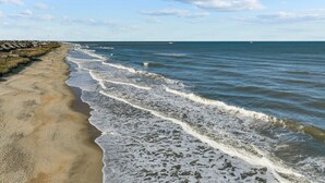 A beach with waves lapping at the shore, a clear sky, and a distant pier. - 3196 - Sea Sights - Oceanfront Duck Condo | Walk to Duck Village (Duck)