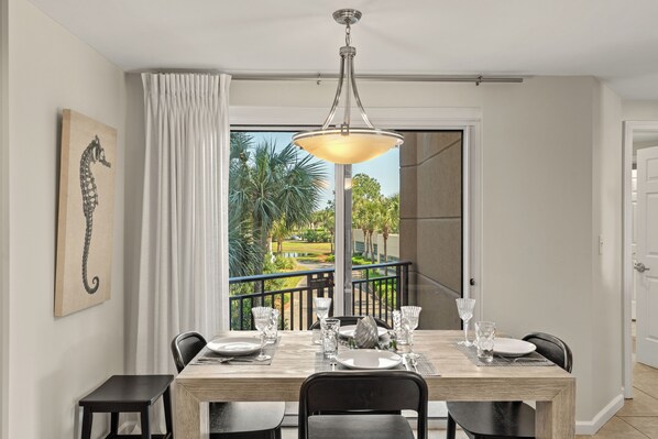 A dining area with a table set for four, a chandelier, and a view of a garden through a glass door.