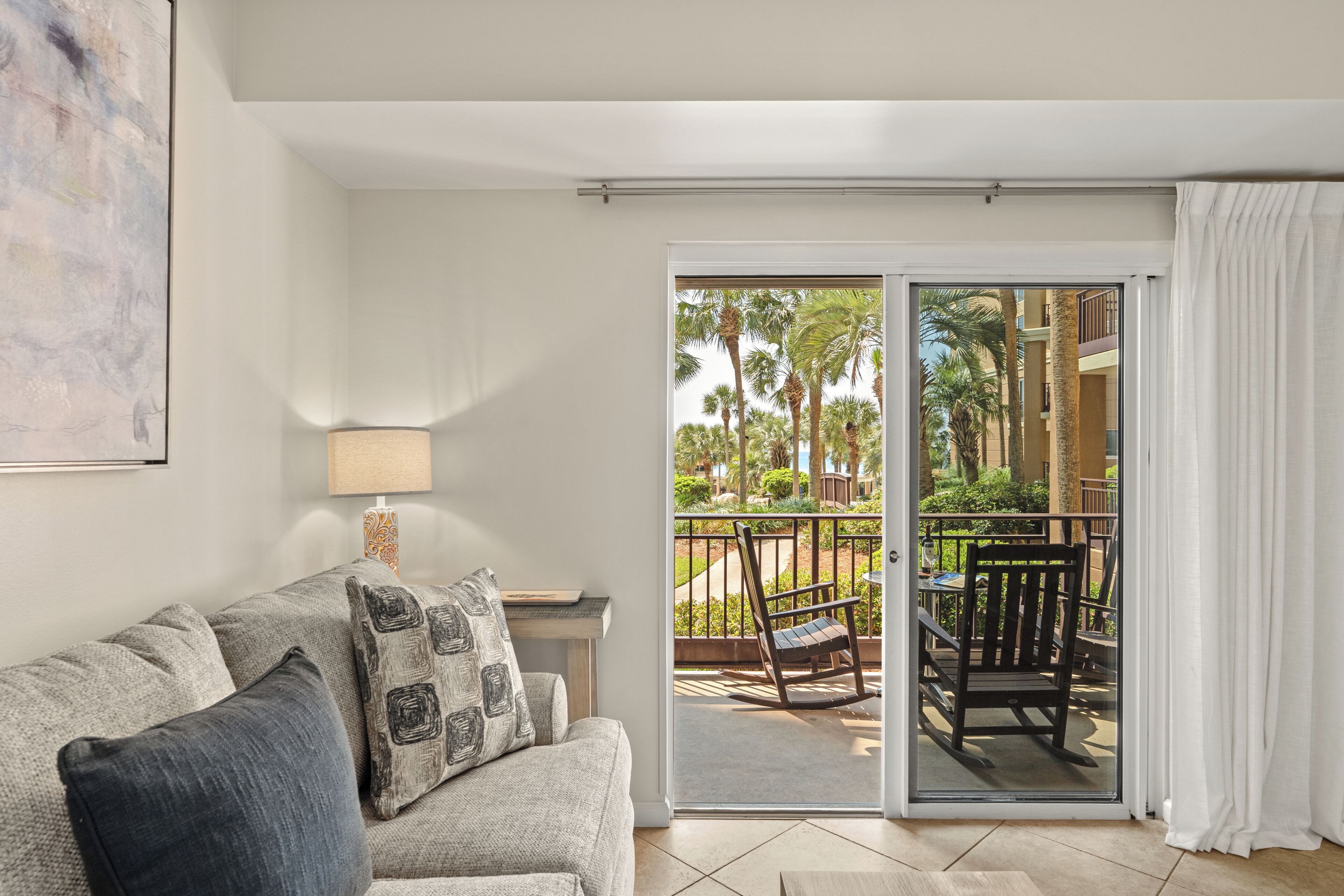 A room with a sofa, a lamp, a sliding glass door to an outdoor area with a chair and table.