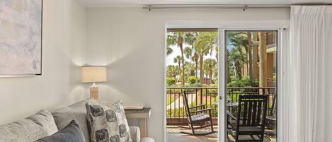 A room with a sofa, a lamp, a sliding glass door to an outdoor area with a chair and table.