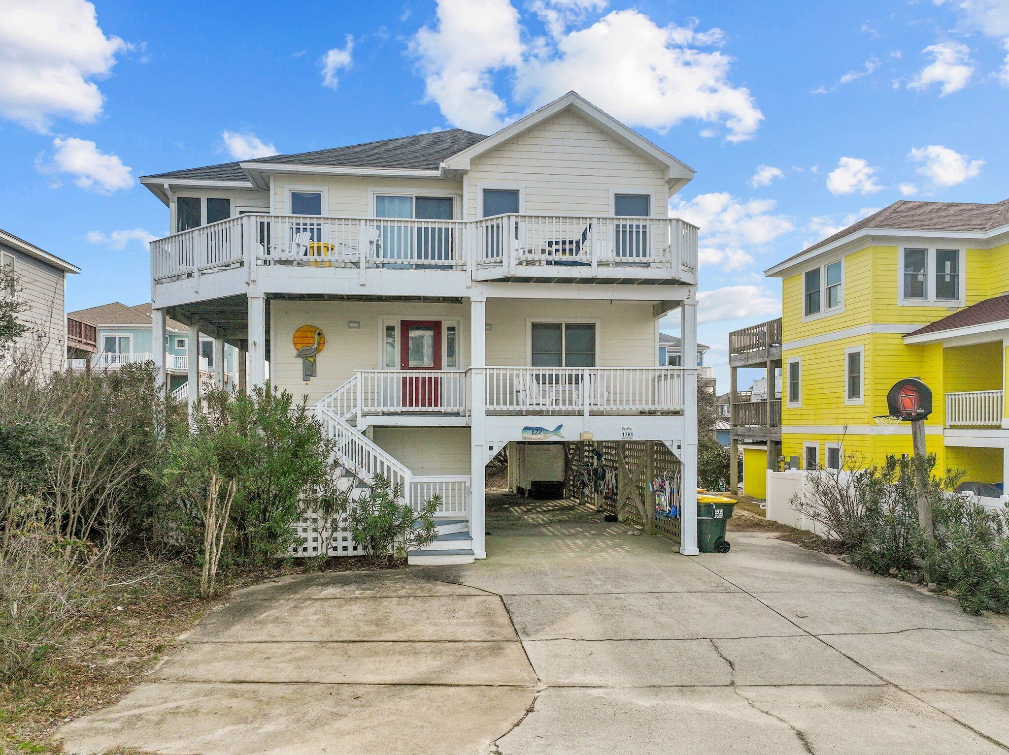 A two-story beachfront house with a balcony, a small porch, and a visible mailbox.