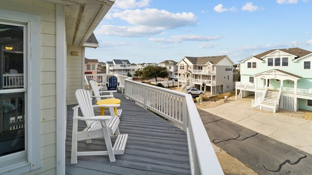 A wooden deck with white chairs and a small table, overlooking a row of houses with a clear sky. - 1781 - Brownie's Retreat, 53 Yards to Beach! Oceanside w/ Private Hot Tub (Corolla)
