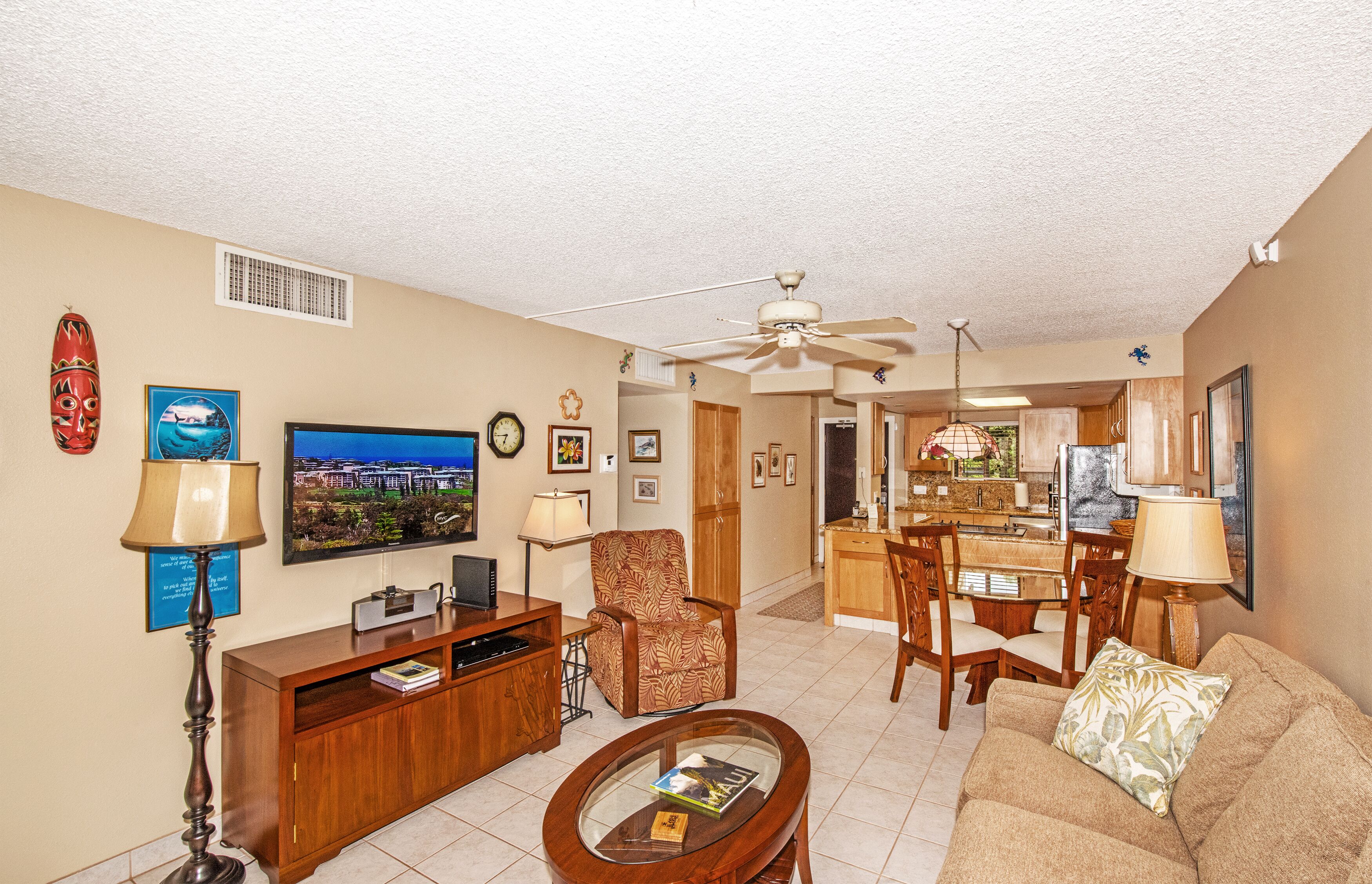 A living room with a sofa, armchair, coffee table, TV, and a dining area with chairs and a table.