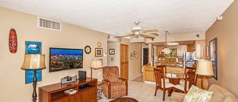 A living room with a sofa, armchair, coffee table, TV, and a dining area with chairs and a table.