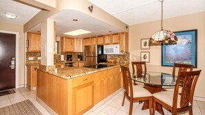 A kitchen with wooden cabinets, a stainless steel refrigerator, a microwave, and a glass dining table with chairs.
