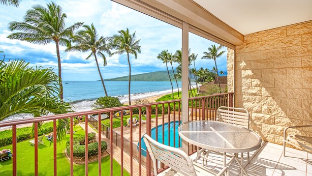 A balcony with a glass railing, a pool, and a view of the ocean and palm trees.