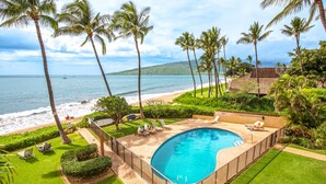 A pool with a view of the ocean, surrounded by palm trees and a well-maintained lawn.