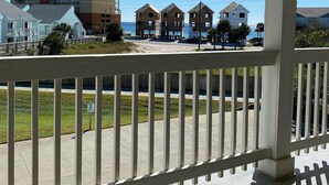 A beachfront property with a covered porch, a view of the ocean, and a tall building in the background.