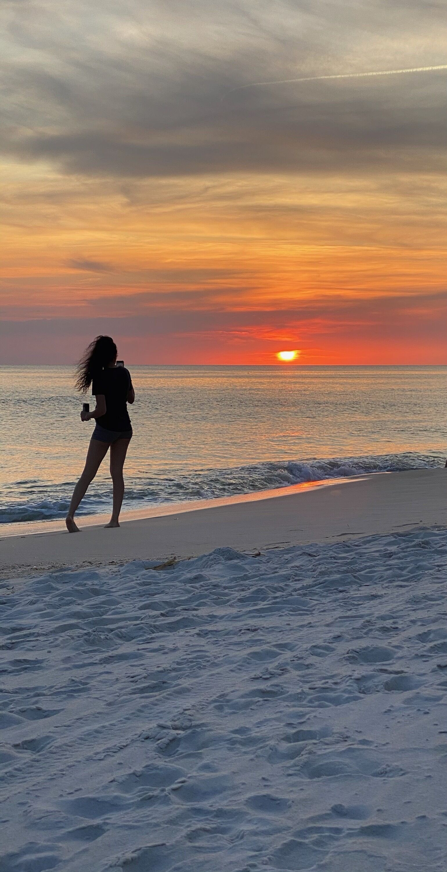 Eine Strandansicht bei Sonnenuntergang, eine Person geht spazieren, und der Himmel ist klar.