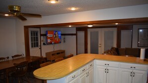 Una cocina con armarios de madera, encimera de madera, ventilador de techo y televisor montado en la pared.