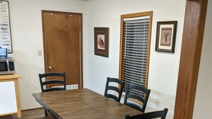 Un comedor con una mesa de madera y cuatro sillas, un banco, un microondas sobre una mesita y cuadros en la pared.