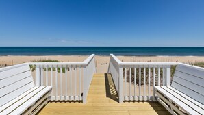 Une terrasse en bois menant à une plage, avec des rampes blanches.