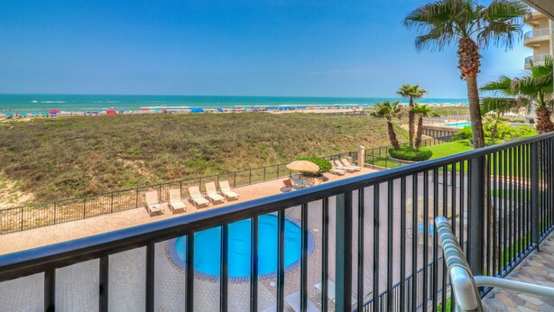 A balcony with a pool, lounge chairs, and a view of the beach and ocean.
