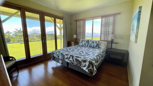 Une chambre avec un lit, un bureau et une vue sur un paysage verdoyant, visible à travers de grandes fenêtres.