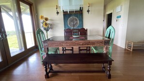Une salle à manger avec une grande table en bois, des chaises vertes, un vase rempli de tournesols et un élément décoratif mural.