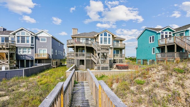 A wooden boardwalk leading to a row of beach houses with multiple stories and balconies. - 5690- Brown Pelican - Spacious Oceanfront Nags Head Retreat (Nags Head)
