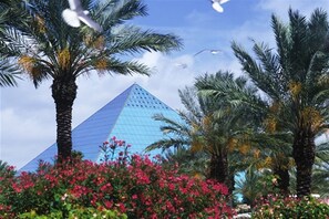 A pyramid surrounded by palm trees and pink flowers.