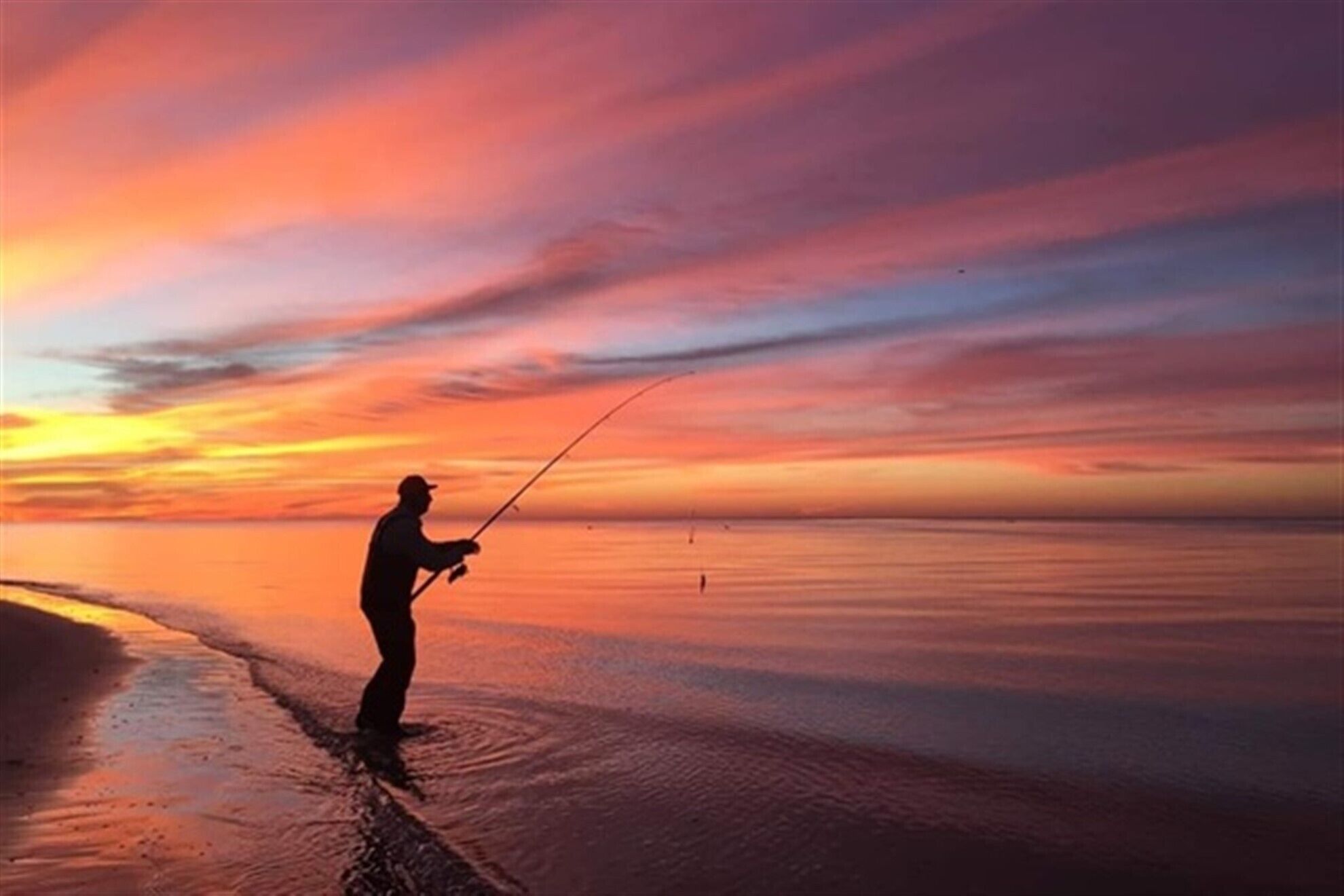 A person fishing at sunset on a beach.